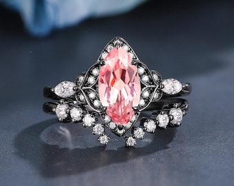 May include: A black engagement ring set featuring a large, marquise-cut pink gemstone. The main ring is accented with small white gemstones and a decorative filigree design. The set includes a matching band with additional white gemstones.