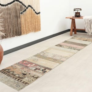 Op de afbeelding: Een lange, rechthoekige vloerkleed met een patchwork ontwerp in neutrale tinten beige, roze en bruin. Het vloerkleed ligt op een lichtgekleurde vloer, met een decoratieve wandophanging en een houten tafel op de achtergrond.