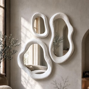 May include: A set of three wall-mounted mirrors featuring irregular, organic shapes and thick, textured white frames. The mirrors are arranged in a cluster, each with a unique, non-symmetrical outline that reflects the surrounding interior space.
