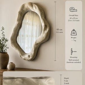 May include: A wall-mounted, irregularly shaped mirror with a textured, off-white frame. The mirror measures 23.6 x 33.5 inches and has a depth of 2 inches. The weight is approximately 15.4 pounds. The handmade mirror includes mounting hardware.