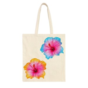 May include: A cream-colored tote bag featuring two vibrant hibiscus flower illustrations. One flower has pink petals with blue edges, and the other has pink petals with yellow edges. The bag has a simple design with two handles.