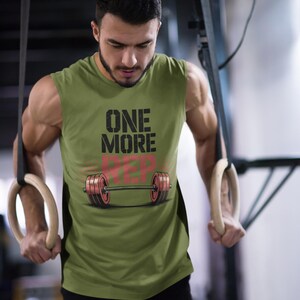 May include: Olive green sleeveless workout shirt with the text "ONE MORE REP" and a barbell graphic. The shirt is worn during a workout with gymnastic rings. The image has a "Summer Vibes" logo in the upper right corner.