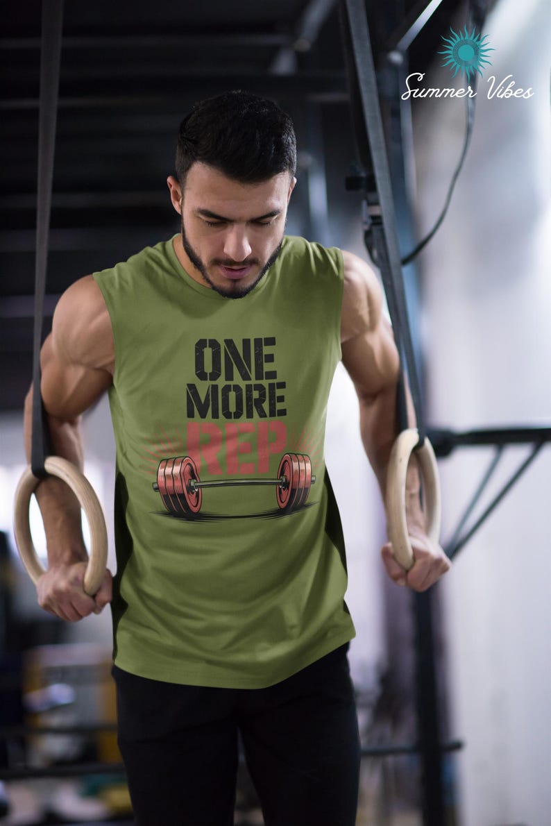 May include: Olive green sleeveless workout shirt with the text "ONE MORE REP" and a barbell graphic. The shirt is worn during a workout with gymnastic rings. The image has a "Summer Vibes" logo in the upper right corner.