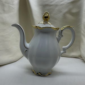 May include: White porcelain teapot with a gold trim and a gold knob on the lid.