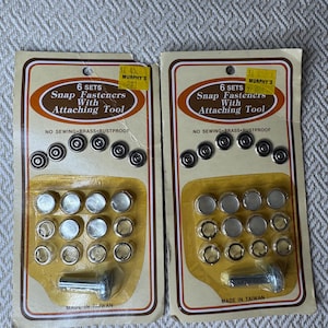 May include: Two identical packages of 6 sets of brass snap fasteners with an attaching tool. Each card features the text 6 SETS Snap Fasteners With Attaching Tool, NO SEWING BRASS RUSTPROOF, and MADE IN TAIWAN. The fasteners are silver-toned metal.