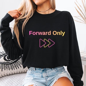 May include: Black sweatshirt with the text "Forward Only" in a gradient of pink, yellow, and orange. Below the text are three forward-facing arrows in pink and yellow. The sweatshirt is worn with denim shorts.
