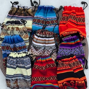 Puede incluir: Una colección de coloridas bolsas con cordón y patrones tejidos. Las bolsas presentan varios diseños en tonos de azul, rojo, amarillo y negro, con motivos geométricos y a rayas. Cada bolsa tiene un cierre de cordón negro.