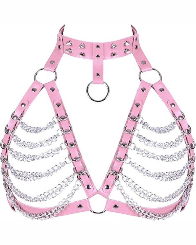 May include: Pink faux leather harness with silver-tone chain and ring accents. The harness features a choker-style collar with studded details and a halter design. The chains drape across the chest, creating a unique and edgy look.