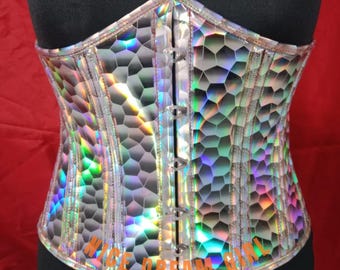 Könnte beinhalten: Holografischer Korsett mit einem geometrischen Wabenmuster. Das Korsett hat eine silberne Oberfläche mit schillernden Regenbogenfarben. Es hat ein strukturiertes Design mit vertikalen Stäbchen und einem Haken- und Ösenverschluss. Der Text "NICE DREAM GIRL" ist unten aufgedruckt.