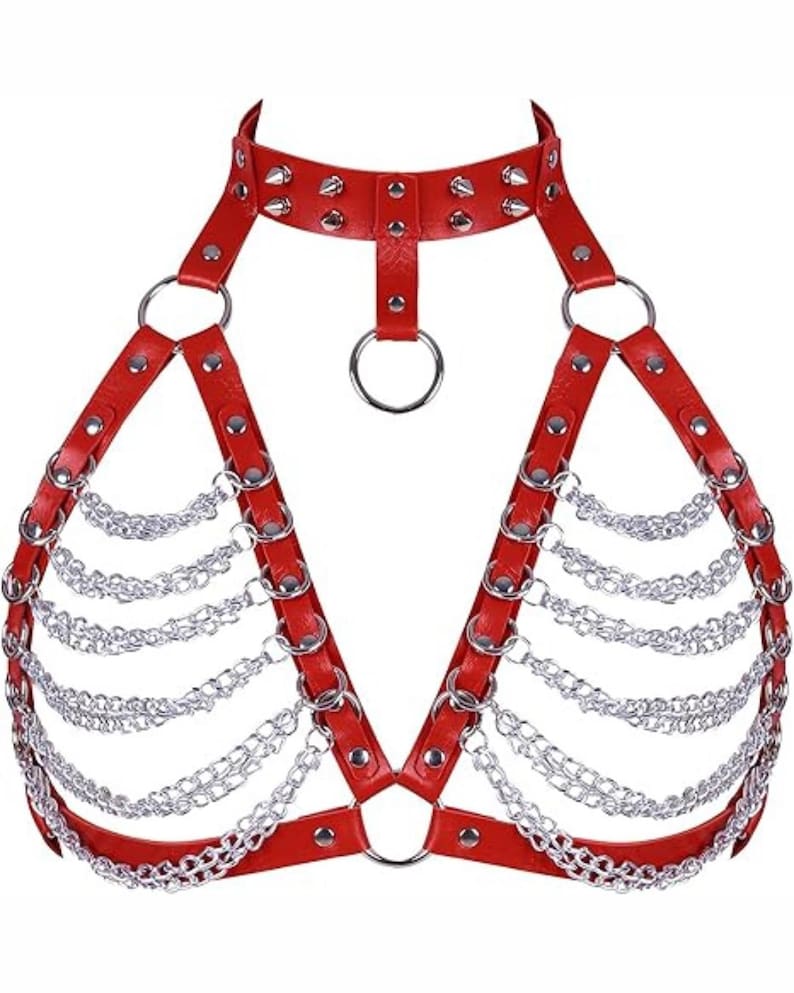 May include: Red leather harness with silver chain detailing. The harness features a choker-style collar with silver studs, connecting to the chest with a central ring. Silver chains hang from the chest straps, creating a layered effect. The harness is designed with multiple adjustable straps.