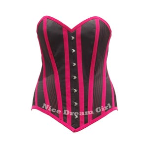 May include: A black and pink striped corset with a sweetheart neckline. The corset has vertical pink stripes and silver-colored clasps down the front. The text "Nice Dream Girl" is printed on the bottom edge.
