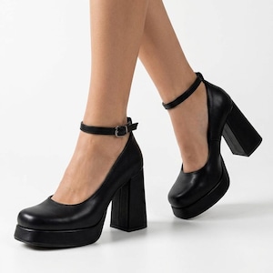 May include: A pair of black platform pumps featuring a square toe, a thick block heel, and a thin ankle strap with a silver-toned metal buckle. The shoes have a smooth finish and a substantial platform sole, providing a solid base and elevation.