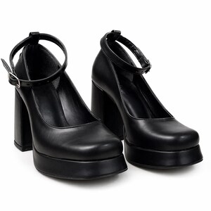May include: A pair of black platform pumps featuring a square toe, a thick block heel, and a thin ankle strap with a silver-toned metal buckle. The shoes have a smooth finish and a substantial platform sole, providing a solid base and elevated height.