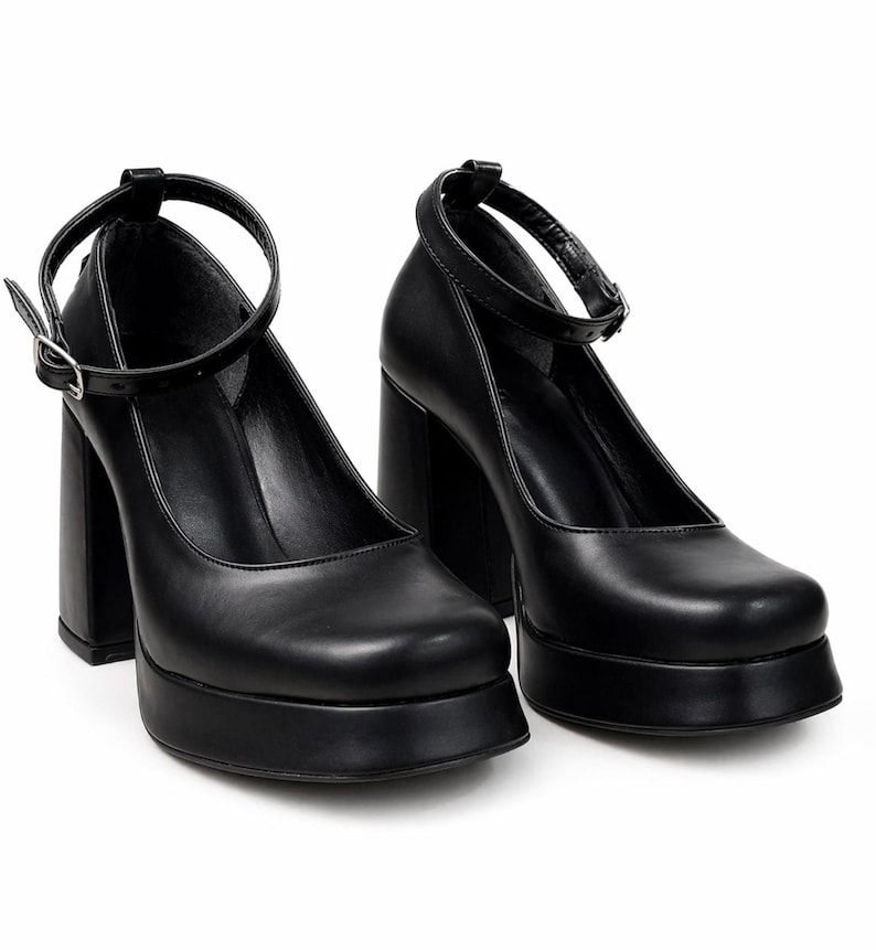 May include: A pair of black platform pumps featuring a square toe, a thick block heel, and a thin ankle strap with a silver-toned metal buckle. The shoes have a smooth finish and a substantial platform sole, providing a solid base and elevated height.