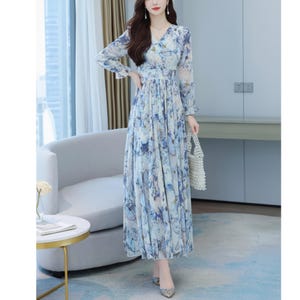 May include: A long, flowing dress with a V-neck and long sleeves. The dress features a blue and white floral pattern and a pleated skirt. The fabric appears lightweight and airy, suitable for warmer weather. The dress is a maxi length.