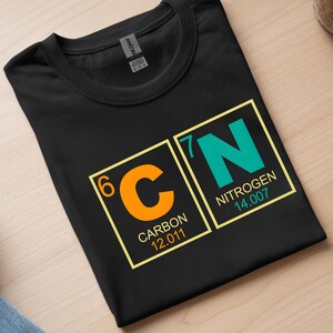 May include: Black t-shirt featuring the periodic table elements Carbon and Nitrogen. The orange 'C' for Carbon is next to the teal 'N' for Nitrogen. The atomic numbers, names, and weights are displayed in yellow boxes.