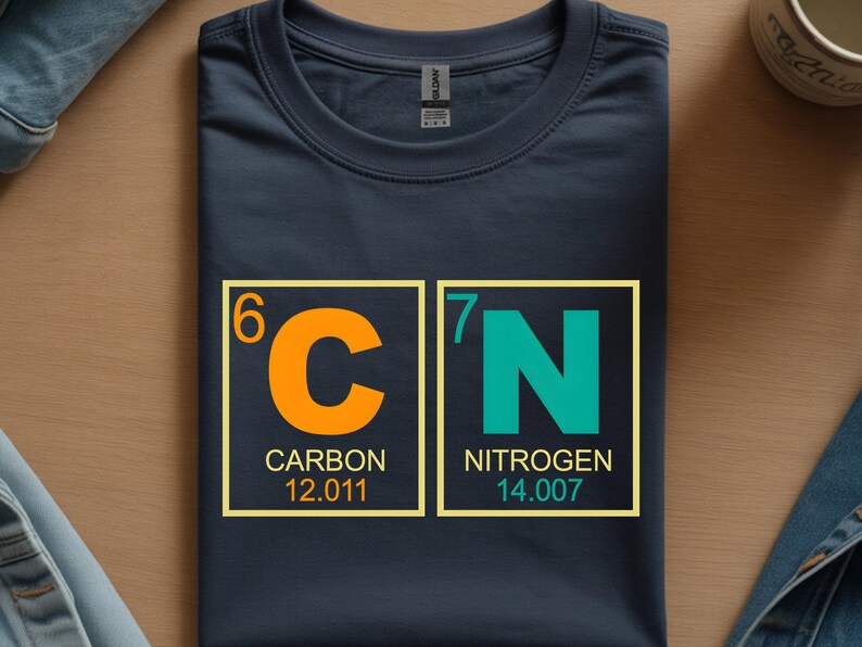 May include: Navy blue t-shirt featuring the chemical symbols for Carbon and Nitrogen. The orange 'C' and teal 'N' are in yellow-bordered boxes, with the atomic numbers and weights below. A science-themed graphic tee.
