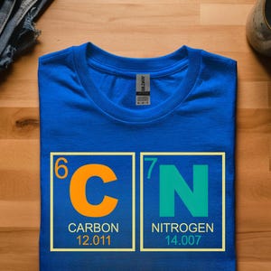 May include: A royal blue t-shirt featuring the periodic table symbols for Carbon and Nitrogen. The orange "C" is in a yellow box with the word "CARBON" and the number 12.011. The green "N" is in a yellow box with the word "NITROGEN" and the number 14.007.