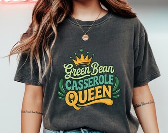 Puede incluir: Camiseta gris oscuro con el texto "Green Bean Casserole Queen" en un diseño colorido con una corona e ilustraciones de judías verdes. La camiseta es de un estilo cómodo e informal.