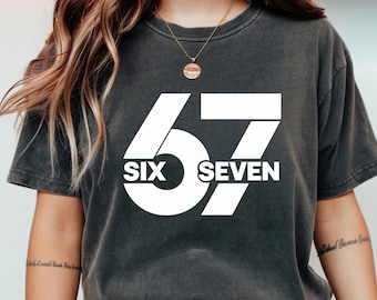 May include: Dark gray t-shirt with the number 67 in a bold white font. The words "SIX" and "SEVEN" are also displayed in white. The shirt has a vintage, washed look.
