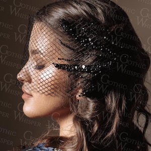 Op de afbeelding: Een vrouw met donker haar draagt een zwarte sluier met een netontwerp en versierd met pailletten. De sluier bedekt een deel van haar gezicht. De afbeelding heeft een gotisch thema, met de woorden "Gothic Whisper" op de achtergrond.