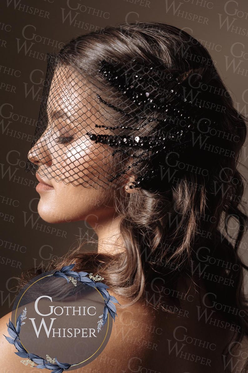 Op de afbeelding: Een vrouw met donker haar draagt een zwarte sluier met een netontwerp en versierd met pailletten. De sluier bedekt een deel van haar gezicht. De afbeelding heeft een gotisch thema, met de woorden "Gothic Whisper" op de achtergrond.