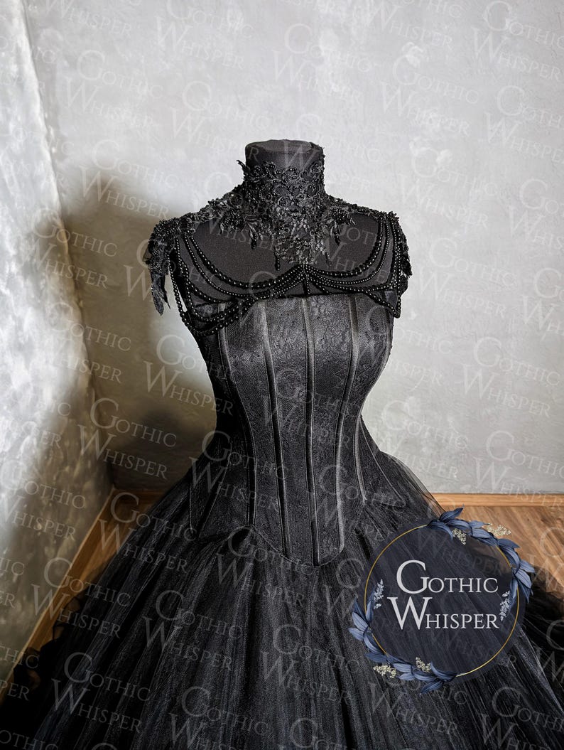 K&ouml;nnte beinhalten: Ein schwarzes Kleid im Gothic-Stil mit hohem Kragen und Korsett-Oberteil. Das Kleid hat aufwendige Spitzen- und Perlenverzierungen am Kragen und an den Schultern. Der volle Rock besteht aus T&uuml;llschichten. Der Text "Gothic Whisper" ist enthalten.