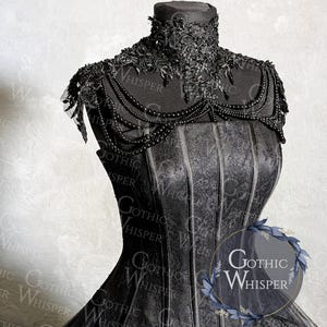 K&ouml;nnte beinhalten: Schwarzes Kleid im Gothic-Stil auf einer Schaufensterpuppe. Das Kleid hat einen hohen, verzierten Kragen, Perlenverzierungen und ein strukturiertes Oberteil. Der Rock besteht aus T&uuml;llschichten. Der Text "Gothic Whisper" ist sichtbar.