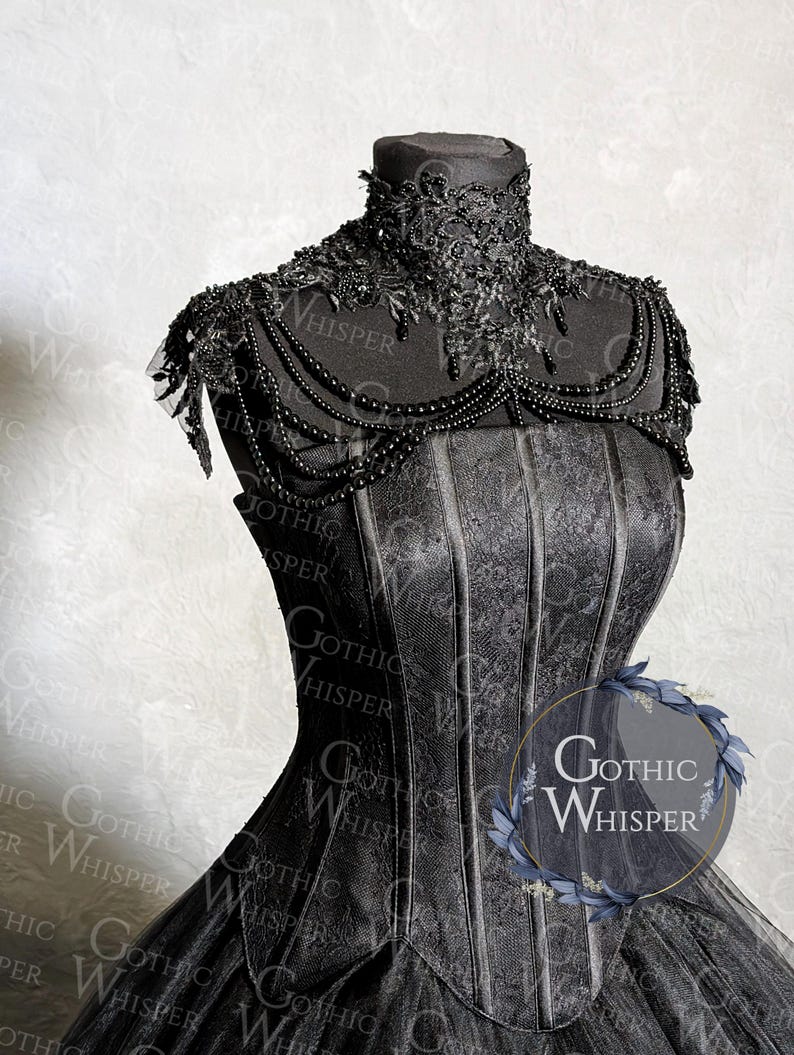 K&ouml;nnte beinhalten: Schwarzes Kleid im Gothic-Stil auf einer Schaufensterpuppe. Das Kleid hat einen hohen, verzierten Kragen, Perlenverzierungen und ein strukturiertes Oberteil. Der Rock besteht aus T&uuml;llschichten. Der Text "Gothic Whisper" ist sichtbar.