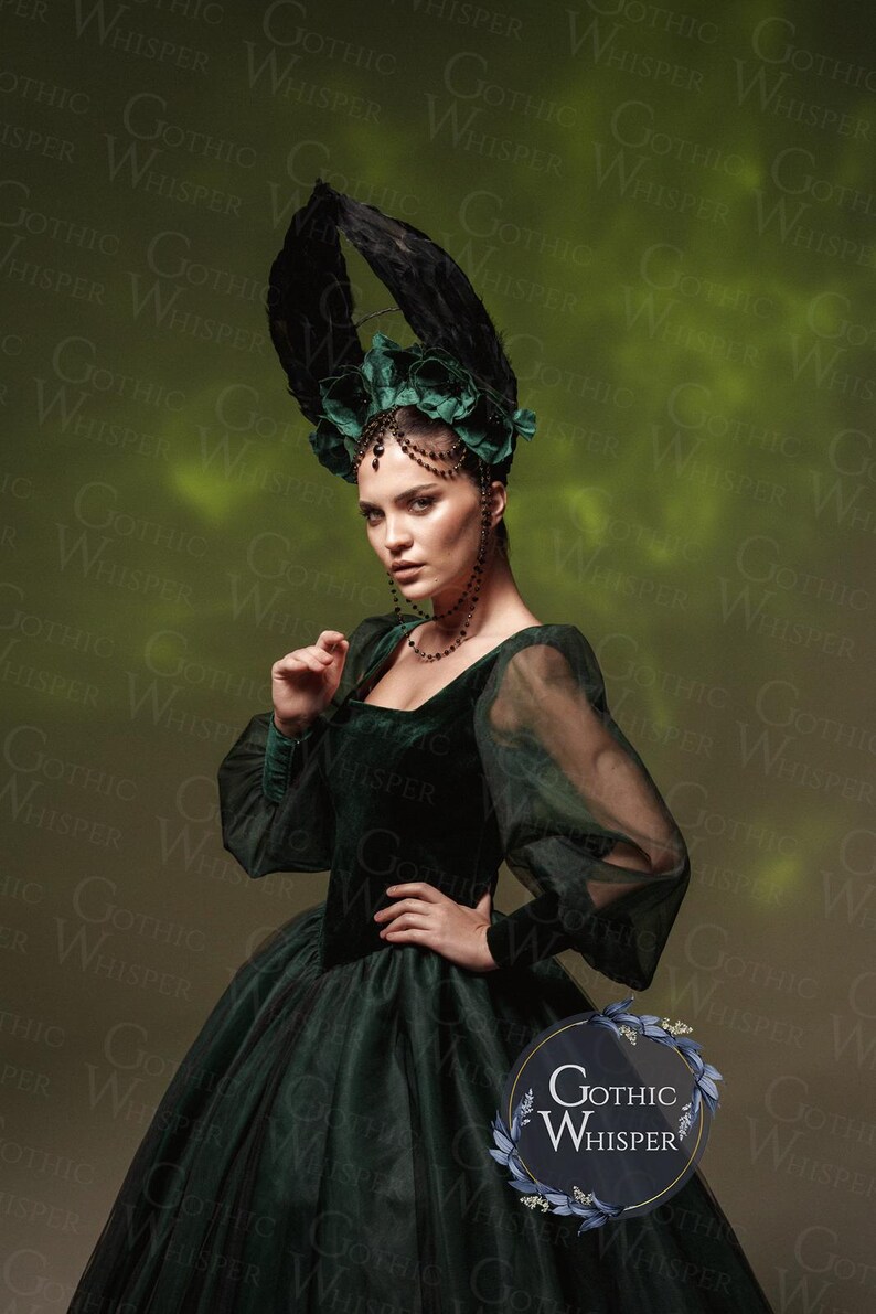 K&ouml;nnte beinhalten: Eine Frau in einem dunkelgr&uuml;nen Samtkleid mit einem durchsichtigen &Uuml;berwurf und einem gro&szlig;en schwarzen Federkopfschmuck. Das Kleid hat ein tailliertes Oberteil und einen vollen Rock. Der Kopfschmuck ist mit gr&uuml;nen Stoffblumen und schwarzen Perlen verziert. Die Frau steht vor einem gr&uuml;nen Hintergrund mit dem Text "Gothic Whisper" in einem Kreis.