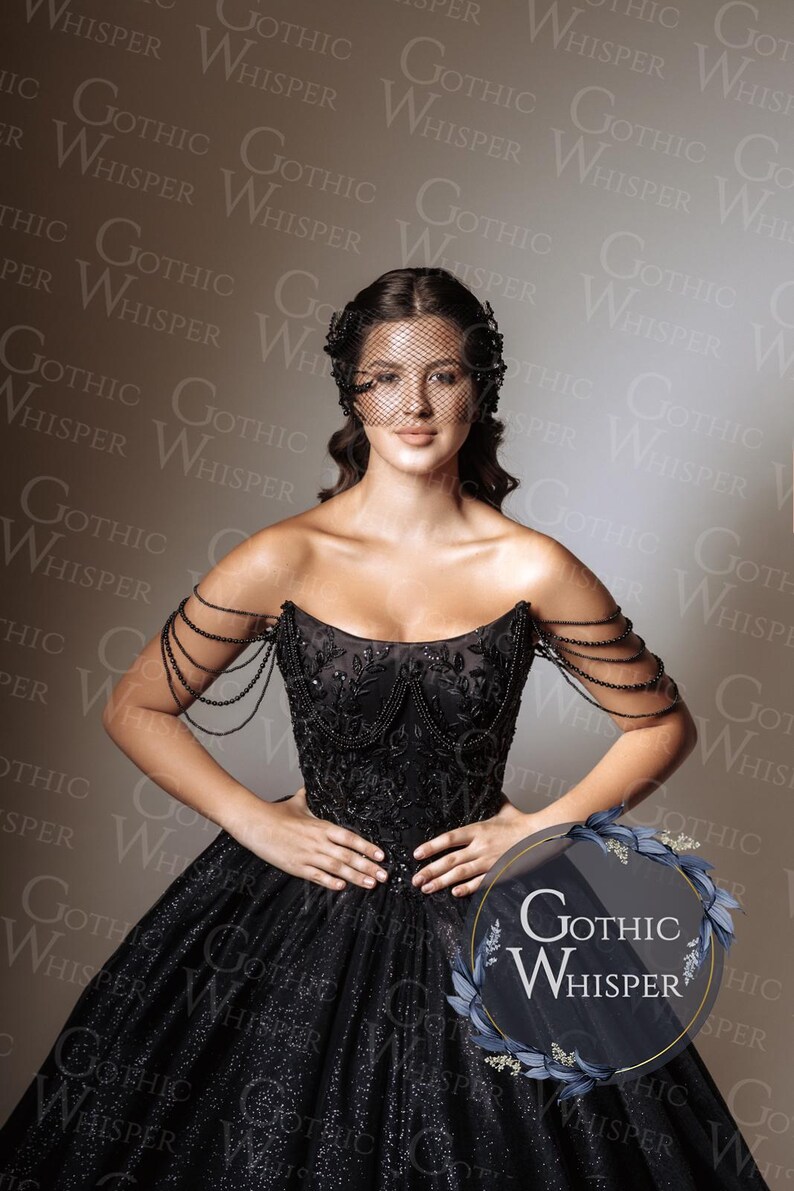 Op de afbeelding: Een zwarte strapless jurk met kralenaccenten en een volle rok. De jurk heeft ingewikkelde borduursels en kralen op de schouders. Een zwarte sluier en het "Gothic Whisper" logo zijn ook zichtbaar.