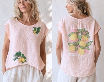 May include: A light pink short-sleeved top featuring a round neckline and a loose fit. The front displays two small lemon branch illustrations. The back features a large rectangular graphic of yellow lemons on green leaves with the text LIMONE.