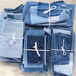 May include: A collection of assorted denim fabric scraps in various shades of blue, ranging from light wash to dark indigo. The fabric pieces are stacked and organized into four distinct bundles, each secured with a simple white string tie.