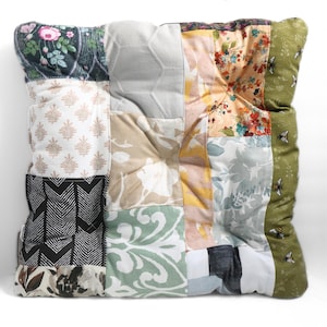 May include: Square patchwork cushion featuring various fabric patterns, including floral, geometric, and botanical designs. The color palette includes shades of green, beige, pink, and black. The cushion is a decorative home accessory.