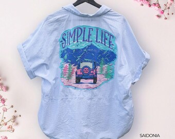 May include: A light blue and white pinstriped short-sleeve button-down shirt featuring a large graphic on the back. The graphic depicts a blue off-road vehicle in a mountain landscape with green trees and the text SIMPLE LIFE in purple letters.