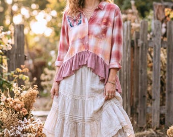 May include: A long-sleeve button-down shirt featuring a red and white plaid pattern, a butterfly graphic on the chest, and a solid mauve ruffled hem. The shirt is paired with a tiered, off-white midi skirt with lace trim detailing at the hem.