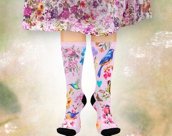 May include: A pair of knee-high socks with a light purple background. The socks feature colorful illustrations of birds, flowers, butterflies, and hearts. The socks have black heels and toes. The overall theme is nature and spring.