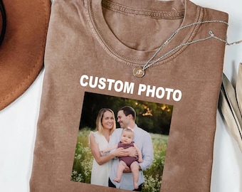 May include: Brown t-shirt with a family photo and the text "CUSTOM PHOTO" in white. The photo shows a family of three in a field. A silver necklace with a pendant is on the shirt.