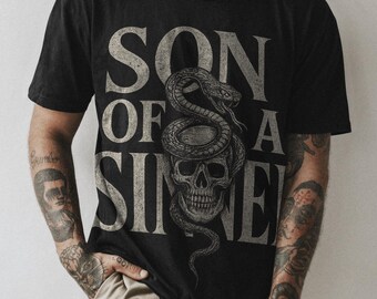 May include: Black t-shirt with a graphic print of a skull with a snake wrapped around it. The text "SON OF A SIN" is printed in white on the shirt.