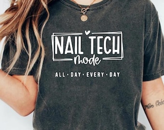 May include: Dark gray t-shirt with the text "NAIL TECH mode ALL DAY EVERY DAY" in a white rectangular design. The shirt has short sleeves and a crew neck.