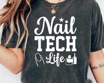 May include: Dark gray t-shirt with the words "Nail TECH Life" in white, along with nail art and polish bottle graphics. The shirt has a crew neck and short sleeves, perfect for casual wear.