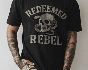 May include: Black t-shirt with a graphic of a skull with a snake wrapped around it. The text "REDEEMED REBEL" is printed on the shirt.