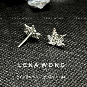 May include: Silver maple leaf stud earrings. The earrings are detailed with leaf veins and have a post backing. The image also includes the text "LENA WONG Art Jewelry Design".