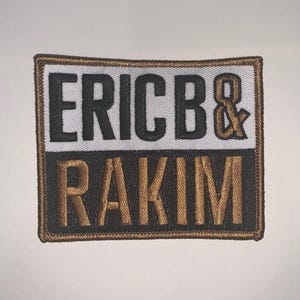 May include: Rectangular patch with the text "ERIC B & RAKIM" in black and gold embroidery. The patch has a white and black background with a brown border.