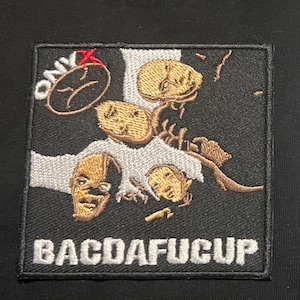 Puede incluir: Parche bordado con fondo negro. Presenta un diseño de rostros estilizados en oro y blanco, con la palabra "ONYX" y un símbolo de cara triste. El texto "BACDAFUCUP" se muestra en la parte inferior.