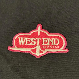 May include: Embroidered patch with the words "WEST END RECORDS" in white lettering on a red background. The patch has a white border and a unique shape, possibly for a jacket or bag.