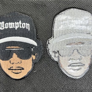 May include: Two embroidered patches featuring a stylized face wearing sunglasses and a cap. One patch is black with the word "Compton" in white. The other patch is gray.