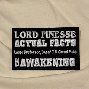 Puede incluir: Un parche rectangular negro bordado con texto blanco que dice LORD FINESSE ACTUAL FACTS, seguido de Large Professor, Sadat X & Grand Puba, y la palabra THE AWAKENING en un tamaño de fuente más grande en la parte inferior.
