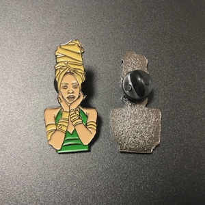 Puede incluir: Pin esmaltado que representa una persona estilizada con un turbante amarillo y una parte superior verde. El pin tiene detalles dorados y un reverso negro. El pin mide aproximadamente 3,8 cm de alto.