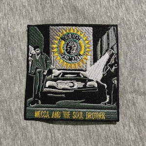 May include: Embroidered patch featuring a man in a green suit standing next to a black car. A large sun-like design is above the car. The text "MECCA AND THE SOUL BROTHER" is at the bottom in gold lettering. The patch is square with a black border.